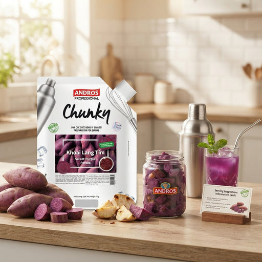 Andros Chunky purple sweet potato sauce mix shown in a kitchen setting with a shaker bottle, a jar of sliced purple sweet potatoes, a prepared drink, and raw sweet potatoes on a wooden counter.